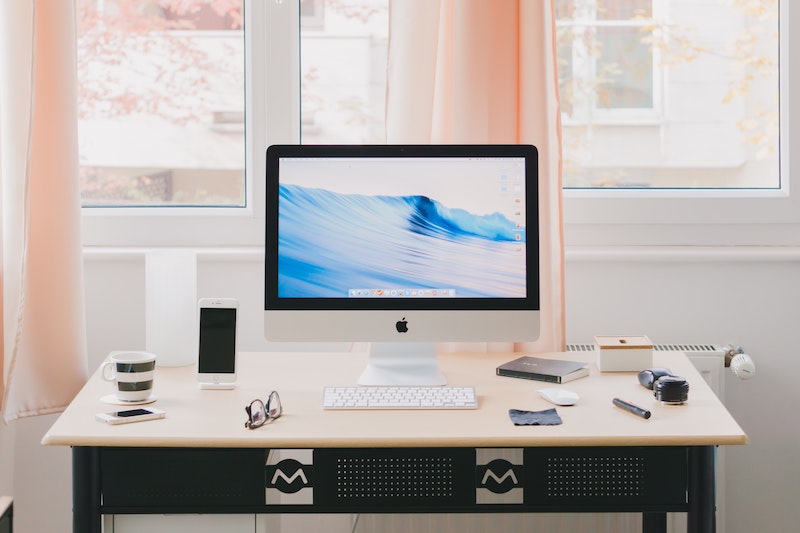 A computer on a desk, surrounded by office supplies and a coffee cup